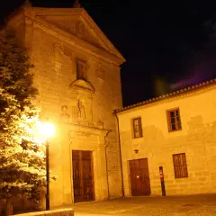 Edificio de piedra iluminado de noche, con un árbol y la luna en el cielo.