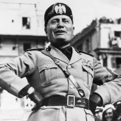 Benito Mussolini, con uniforme militar y gorra, sonríe ante una multitud. Su ascenso al poder es un capítulo oscuro de la historia.