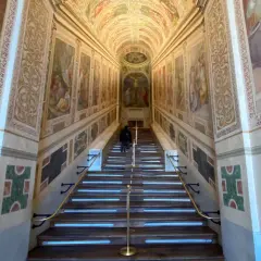 Persona subiendo la escalera santa de Roma, con frescos en las paredes y una crucifixión al final.