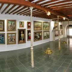 Galería de arte con cuadros y esculturas, techos de madera y suelo de baldosas.