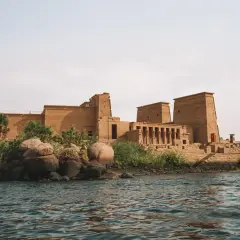 Antiguo templo egipcio en una isla, con el Nilo en primer plano. La imponente arquitectura de la presa de Asuán se alza majestuosa.