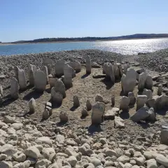 El dolmen de Guadalperal emerge de las aguas bajas, un círculo de piedras ancestrales bajo un cielo azul.