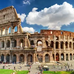 El **Coliseo de Roma**, imponente anfiteatro romano, recibe a turistas bajo un cielo azul con nubes.