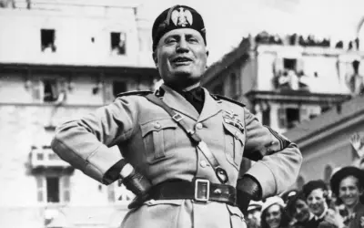 Benito Mussolini, con uniforme militar y gorra, sonríe ante una multitud. Su ascenso al poder es un capítulo oscuro de la historia.