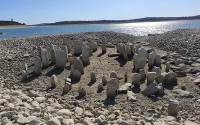 El dolmen de Guadalperal emerge de las aguas bajas, un círculo de piedras ancestrales bajo un cielo azul.