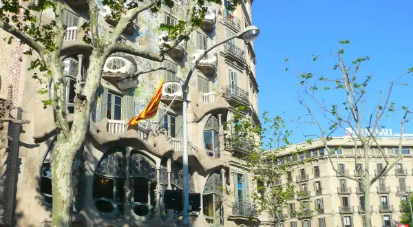 La Casa Batlló, joya modernista, luce su fachada ondulante y colorida bajo el sol. Una bandera catalana ondea, celebrando Sant Jordi.