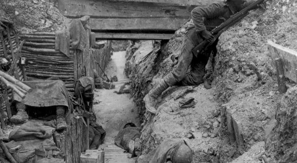 Soldado en posición de combate en las trincheras de la Primera Guerra Mundial. Otros soldados descansan o duermen en el fondo.