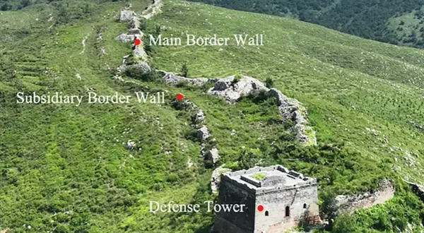 La muralla china se extiende por colinas verdes, con una torre de defensa y muros principales y subsidiarios.