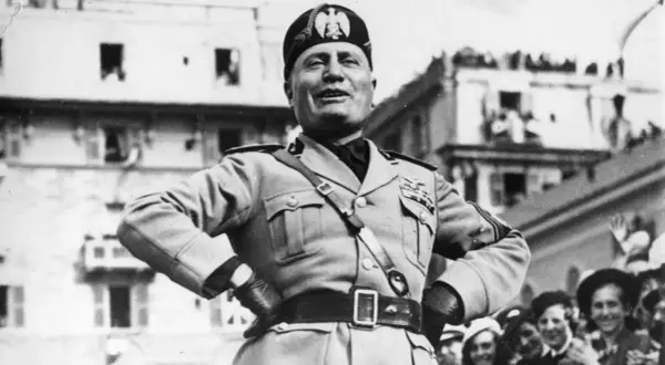 Benito Mussolini, con uniforme militar y gorra, sonríe ante una multitud. Su ascenso al poder es un capítulo oscuro de la historia.
