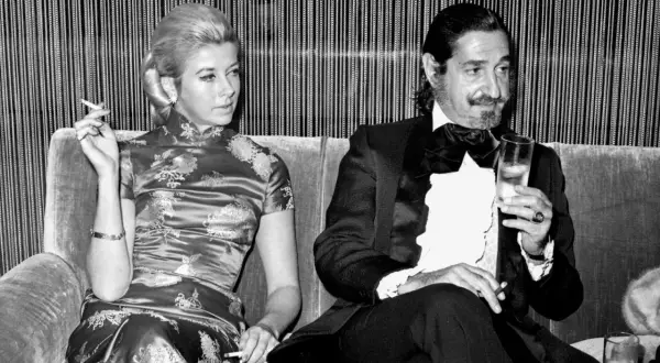 Jaime de Mora y Aragón, elegante en esmoquin, brinda con una copa mientras una mujer con vestido oriental fuma.