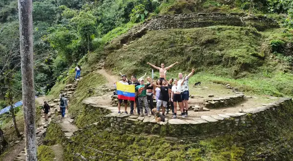Grupo de turistas celebra en la **ciudad perdida Colombia**, rodeados de ruinas ancestrales y exuberante vegetación.