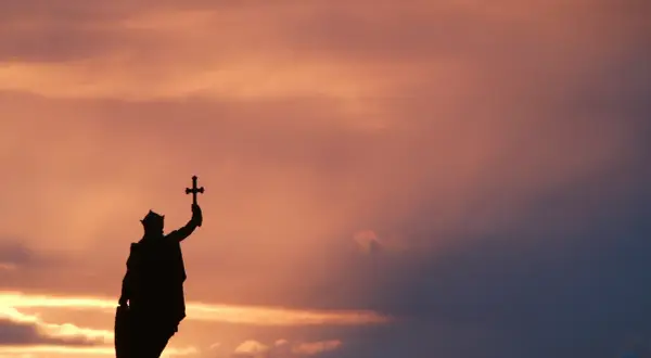 Silueta de estatua con cruz alzada, evocando la gesta de Don Pelayo y la Reconquista, bajo un cielo crepuscular.