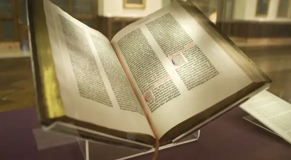 Un antiguo libro abierto, que podría ser la biblia, con páginas llenas de texto y decoraciones.