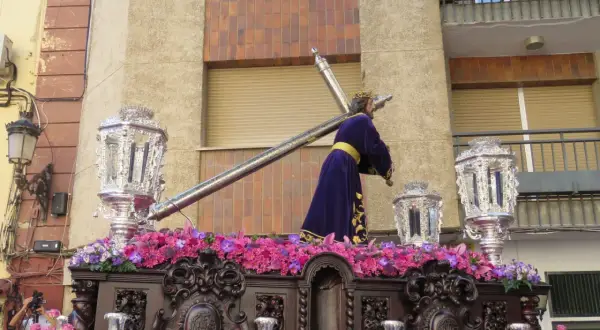 Procesión de Semana Santa con imagen de Jesús portando la cruz, adornada con flores y candelabros. Obra de Amadeo Ruiz Olmos.