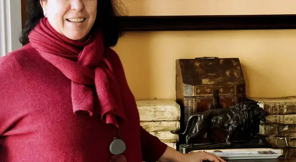 Una mujer sonríe junto a una estatuilla de león y libros antiguos, quizás en un salón de **Loyola de Palacio**.