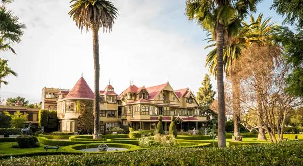 La casa Winchester, una mansión victoriana de colores vivos, se alza entre palmeras y jardines cuidados.