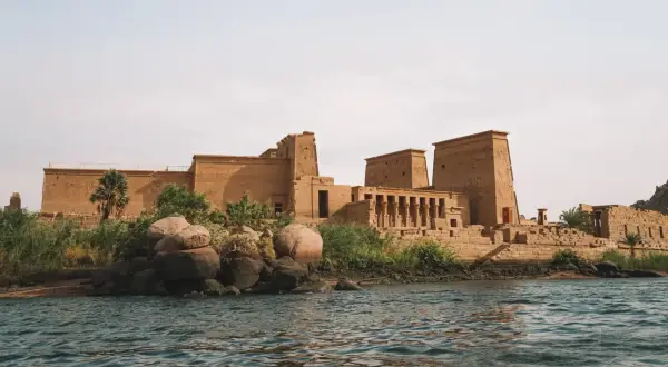 Antiguo templo egipcio en una isla, con el Nilo en primer plano. La imponente arquitectura de la presa de Asuán se alza majestuosa.