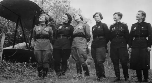 Seis mujeres con uniformes militares posan junto a un biplano. Son las brujas de la noche, listas para volar.