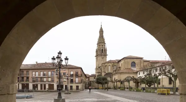 Plaza de Santo Domingo de la Calzada, con su imponente catedral y edificios históricos. Un peregrino con paraguas cruza la plaza empedrada.