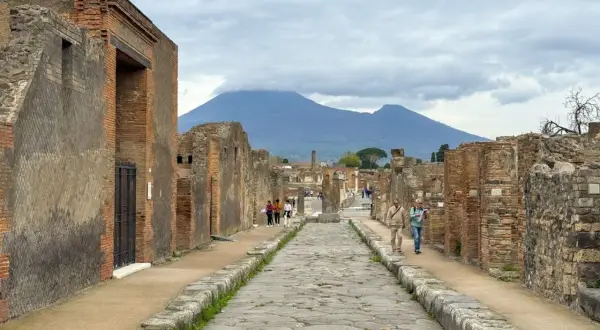 Antigua calle empedrada en el parque arqueológico de Pompeya, con ruinas a ambos lados y el Vesubio al fondo.