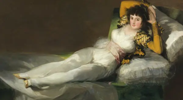 La venus del espejo, una mujer recostada en un diván, viste un traje blanco y mira al espectador con una expresión seductora.