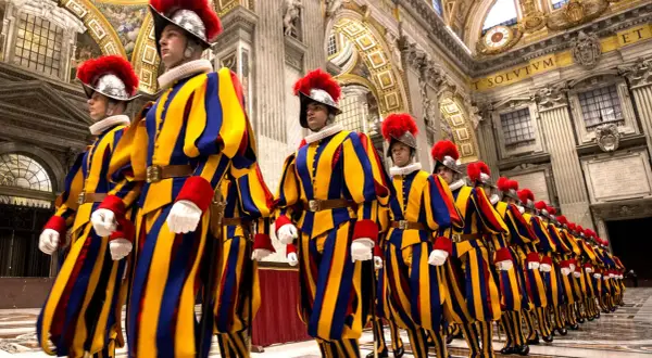 Guardia suiza del Vaticano desfila en formación, con sus icónicos uniformes a rayas amarillas, azules y rojas, y penachos rojos.