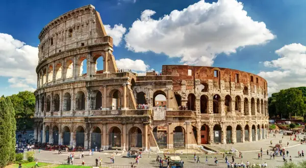 El **Coliseo de Roma**, imponente anfiteatro romano, recibe a turistas bajo un cielo azul con nubes.