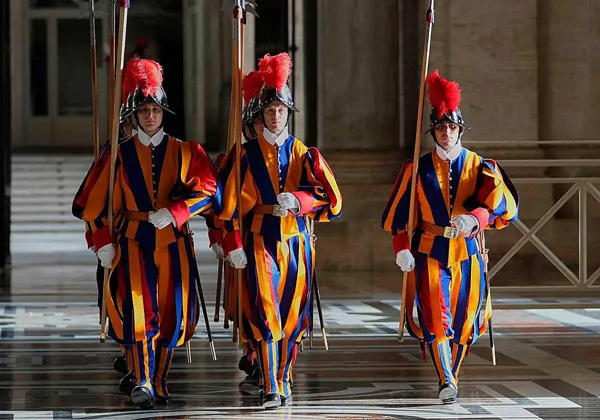Tres miembros de la guardia suiza vaticano, con sus coloridos uniformes, marchan con lanzas.