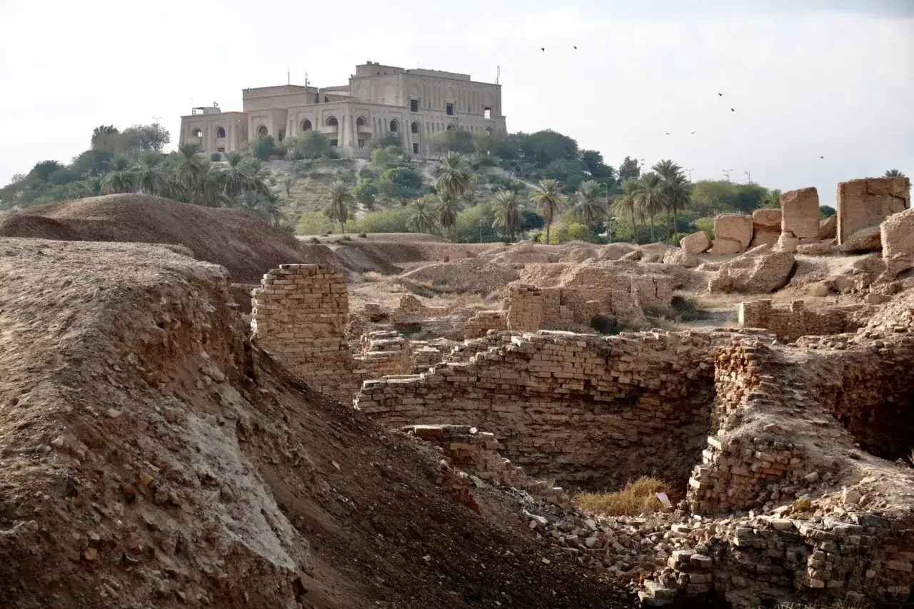 Ruinas de ladrillo y un edificio moderno en una colina, evocando la pregunta: ¿donde esta Babilonia? Palmeras y pájaros en el cielo.