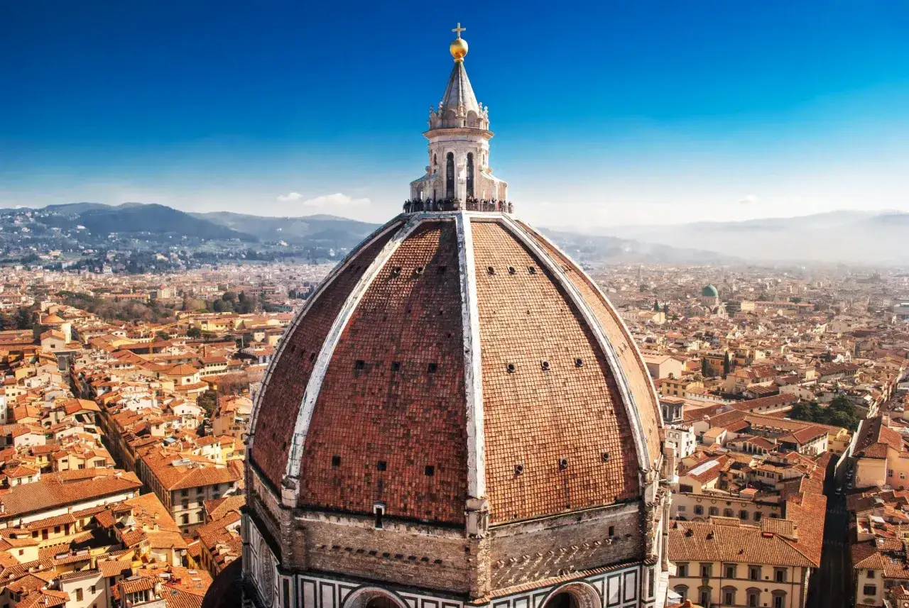 La c&uacute;pula del Duomo de Florencia se alza majestuosa sobre la ciudad, con sus tejados anaranjados y un cielo azul intenso.
