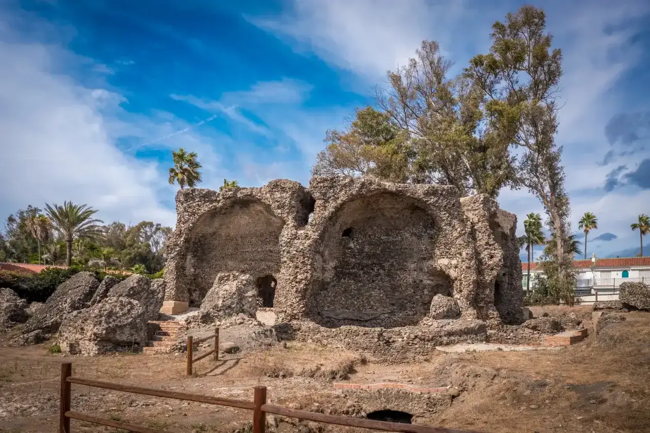 Ruinas de las termas romanas, con arcos de piedra y vegetación exuberante bajo un cielo azul.