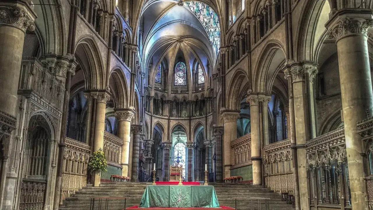 Interior de una majestuosa catedral g&oacute;tica, con arcos elevados, b&oacute;vedas intrincadas y vitrales que iluminan el espacio.