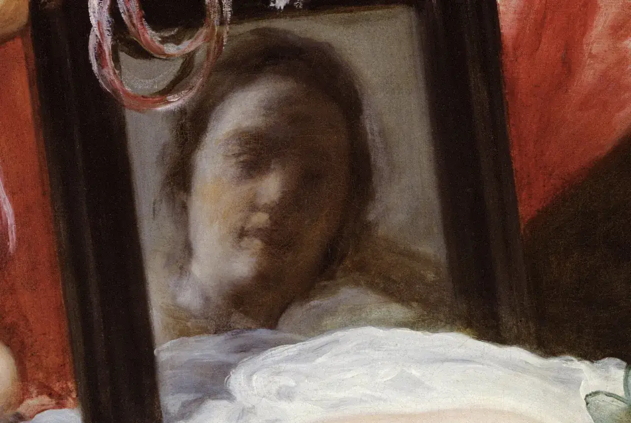 El rostro de la Venus del Espejo se refleja en un espejo, con un velo blanco y cortinas rojas.