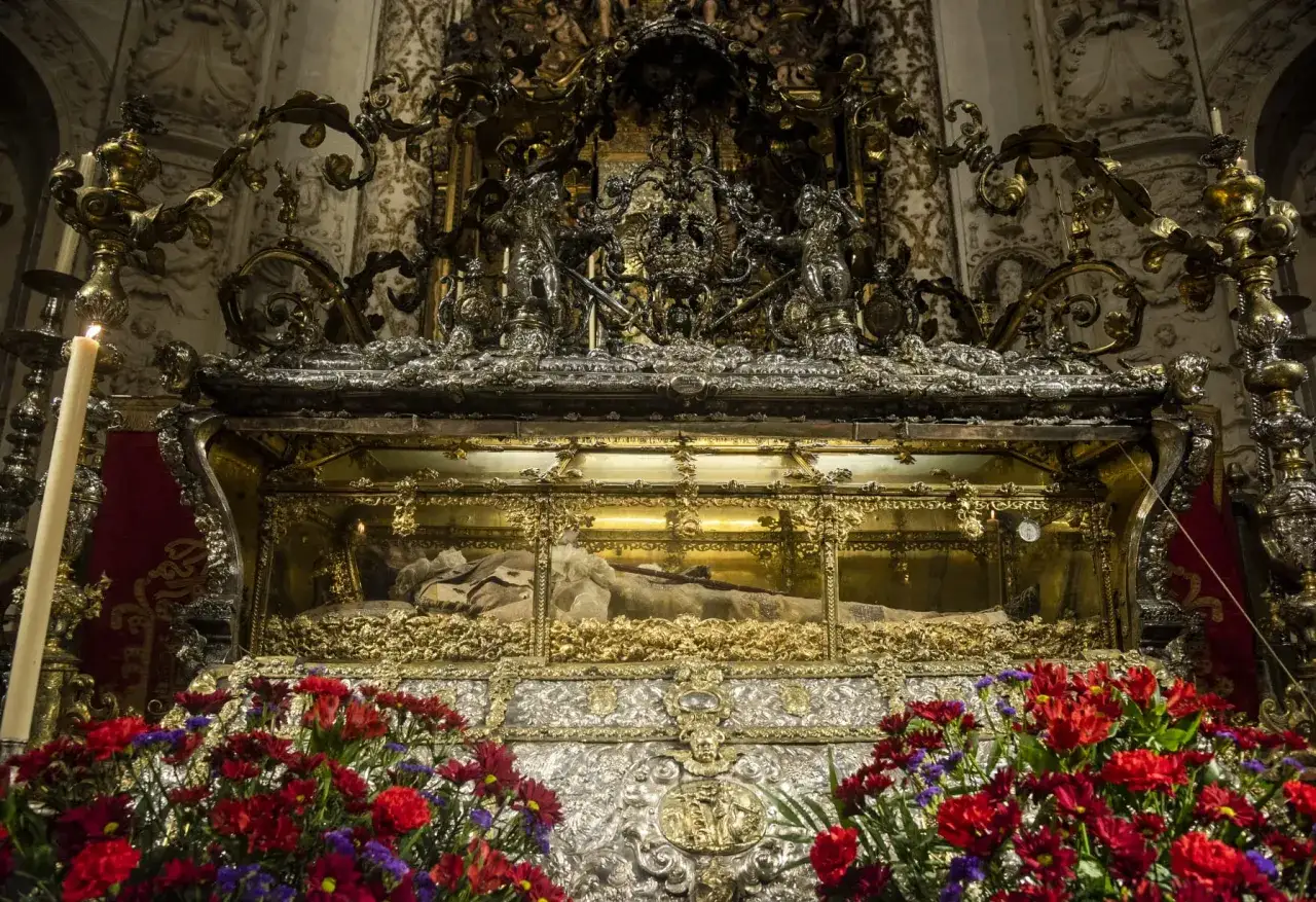 Relicario dorado con el cuerpo de Fernando el Santo, adornado con flores rojas y velas.