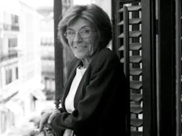 Carmen Rico Godoy, con gafas y chaqueta, mira a la cámara desde un balcón. Parece una escena de "Carmen Rico Godoy abandonada".