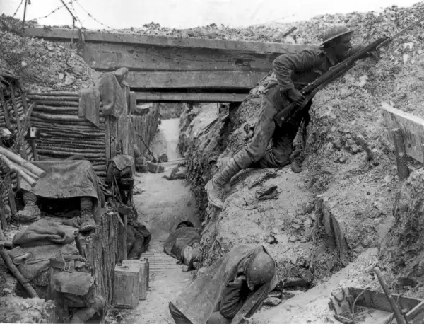 Soldado en posición de combate en las trincheras de la Primera Guerra Mundial. Otros soldados descansan o duermen en el fondo.