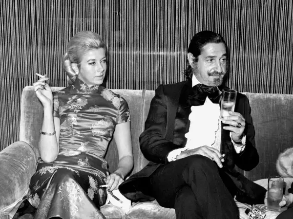 Jaime de Mora y Aragón, elegante en esmoquin, brinda con una copa mientras una mujer con vestido oriental fuma.