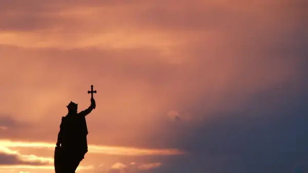 Silueta de estatua con cruz alzada, evocando la gesta de Don Pelayo y la Reconquista, bajo un cielo crepuscular.