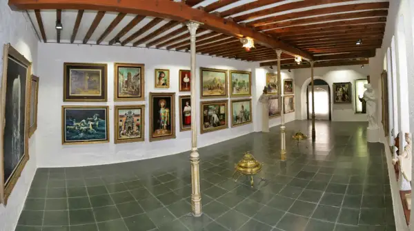 Galería de arte con cuadros y esculturas, techos de madera y suelo de baldosas.