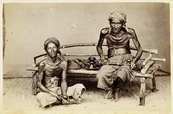 Dos hombres demacrados, víctimas de la guerra del opio, sentados con pipas de opio.