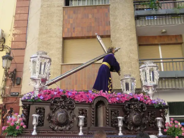 Procesión de Semana Santa con imagen de Jesús portando la cruz, adornada con flores y candelabros. Obra de Amadeo Ruiz Olmos.