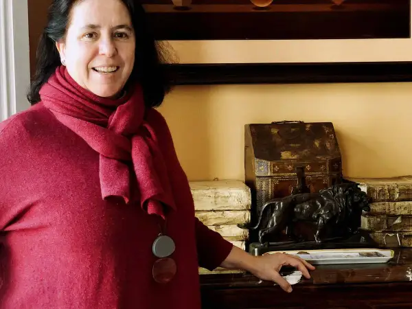 Una mujer sonríe junto a una estatuilla de león y libros antiguos, quizás en un salón de **Loyola de Palacio**.