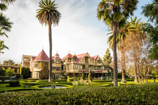 La casa Winchester, una mansión victoriana de colores vivos, se alza entre palmeras y jardines cuidados.