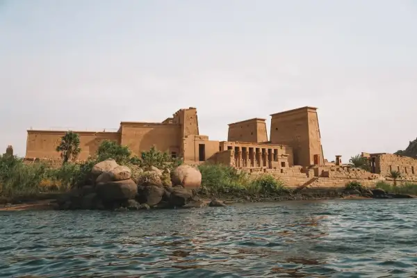 Antiguo templo egipcio en una isla, con el Nilo en primer plano. La imponente arquitectura de la presa de Asuán se alza majestuosa.