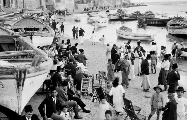 Gente en la playa con barcos, un vistazo al posible origen del conflicto entre Israel y Palestina.