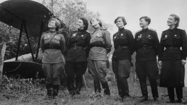 Seis mujeres con uniformes militares posan junto a un biplano. Son las brujas de la noche, listas para volar.