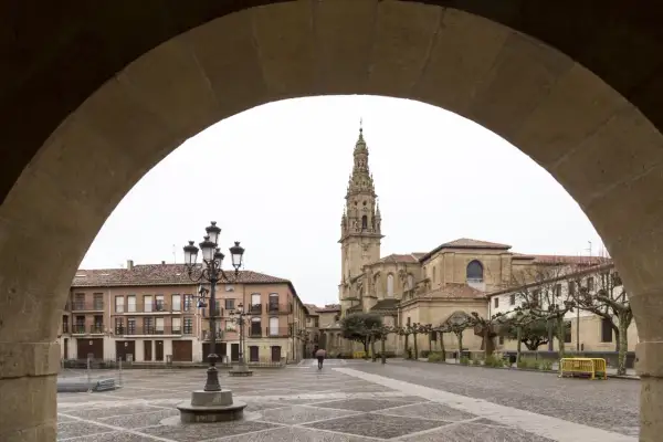 Plaza de Santo Domingo de la Calzada, con su imponente catedral y edificios históricos. Un peregrino con paraguas cruza la plaza empedrada.