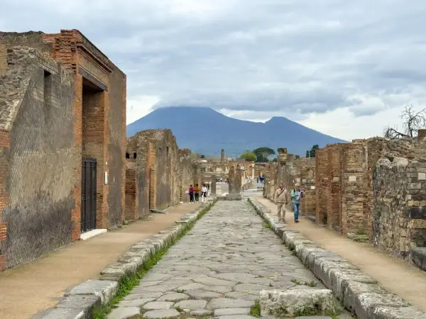 Antigua calle empedrada en el parque arqueológico de Pompeya, con ruinas a ambos lados y el Vesubio al fondo.