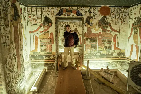 Un hombre posa en la tumba de Nefertari, rodeado de vibrantes jeroglíficos y figuras divinas que narran su viaje al más allá.